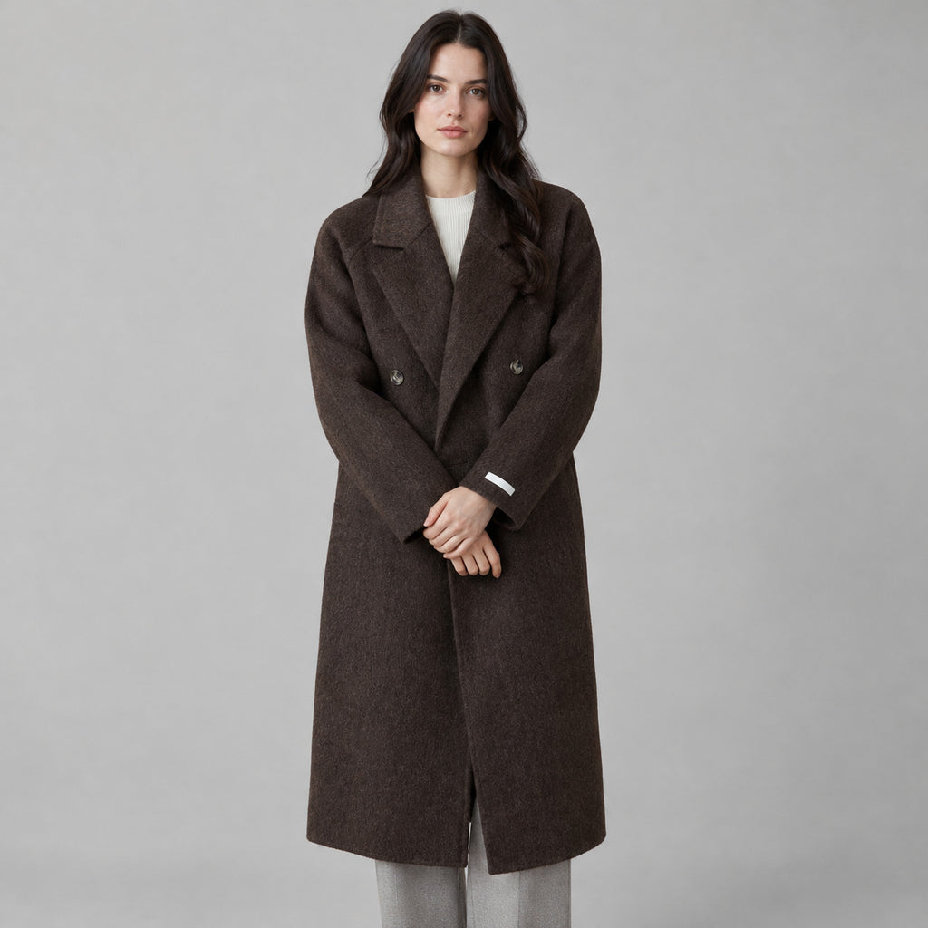 Dark brown double-breasted long wool coat worn by a model against a neutral studio backdrop.
