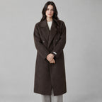 Dark brown double-breasted long wool coat worn by a model against a neutral studio backdrop.