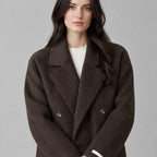 Dark brown double-breasted long wool coat worn, cropped from the shoulders to the waist to show the notched lapels and double-breasted closure.