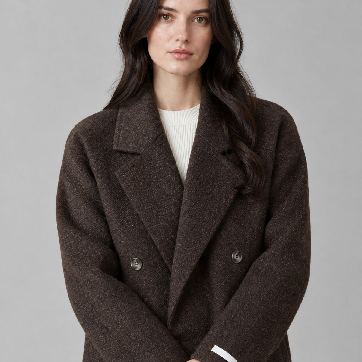 Dark brown double-breasted long wool coat worn, cropped from the shoulders to the waist to show the notched lapels and double-breasted closure.