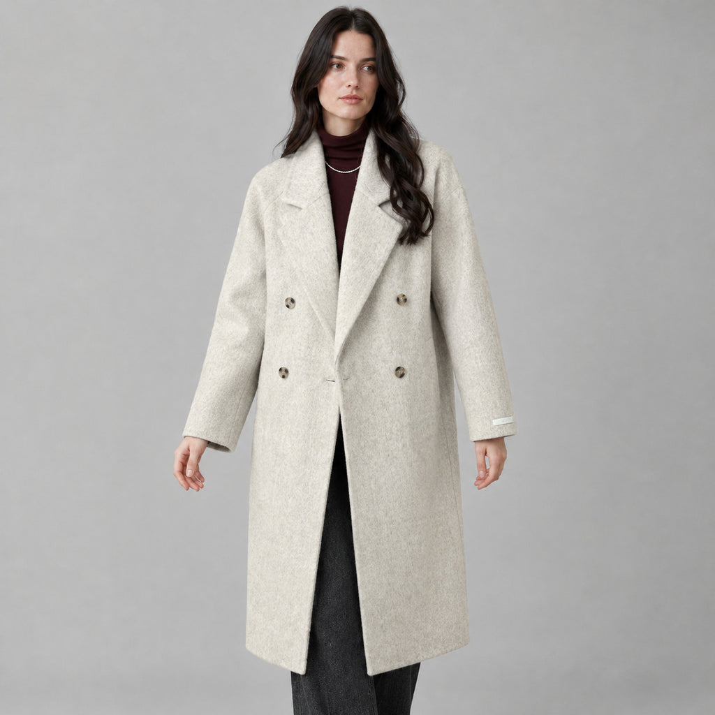 Oatmeal double-breasted long wool coat worn by a model against a neutral studio backdrop.