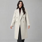 Oatmeal double-breasted long wool coat worn by a model against a neutral studio backdrop.