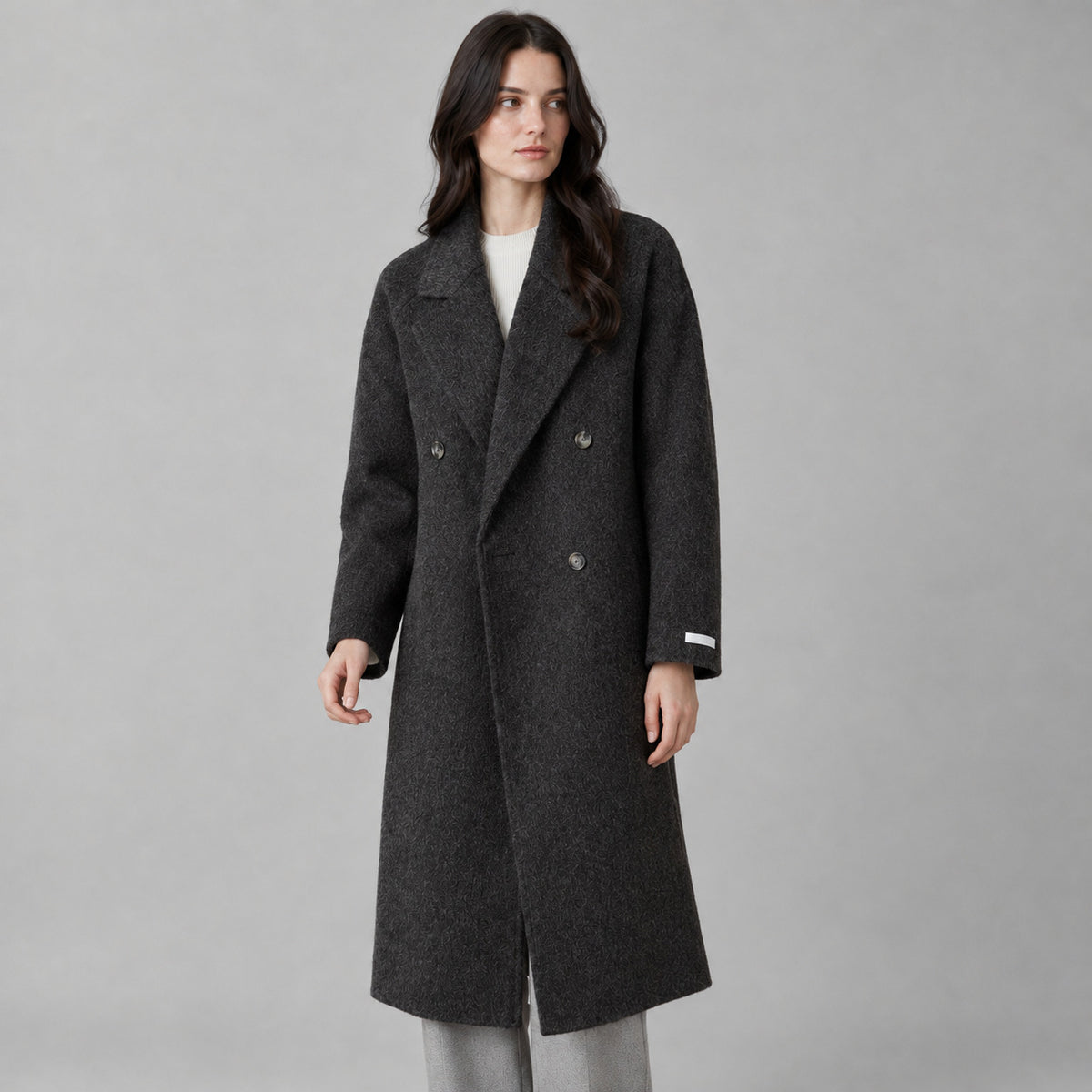 Charcoal gray double-breasted long wool coat worn by a model against a neutral studio backdrop.