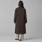 Back of the dark brown double-breasted long wool coat worn, showing the centre back seam.