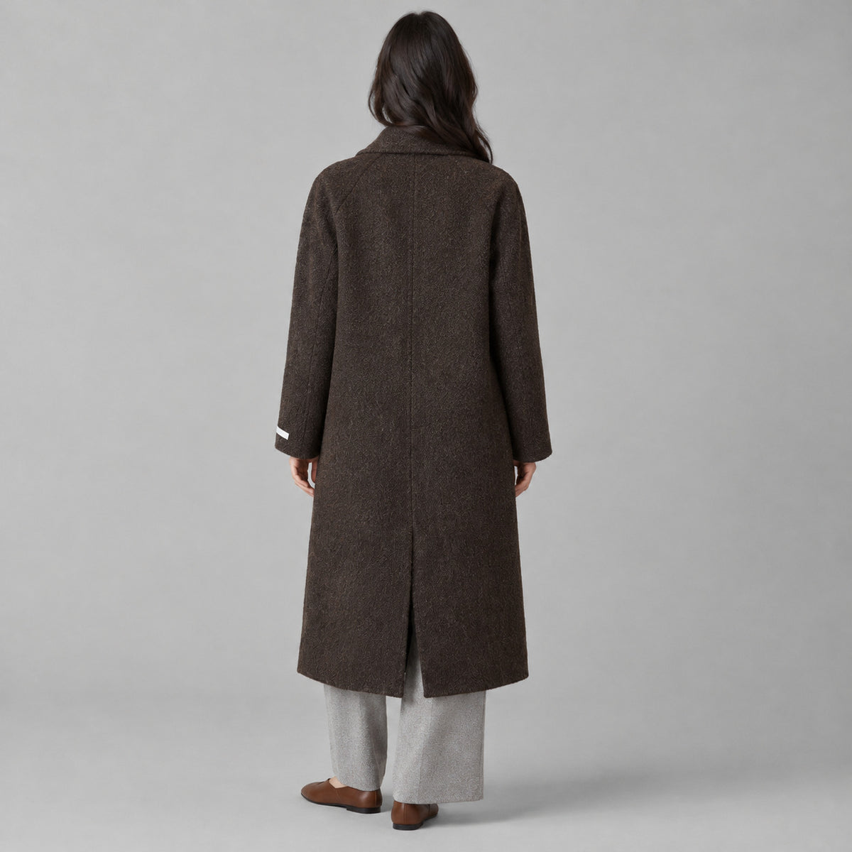 Back of the dark brown double-breasted long wool coat worn, showing the centre back seam.