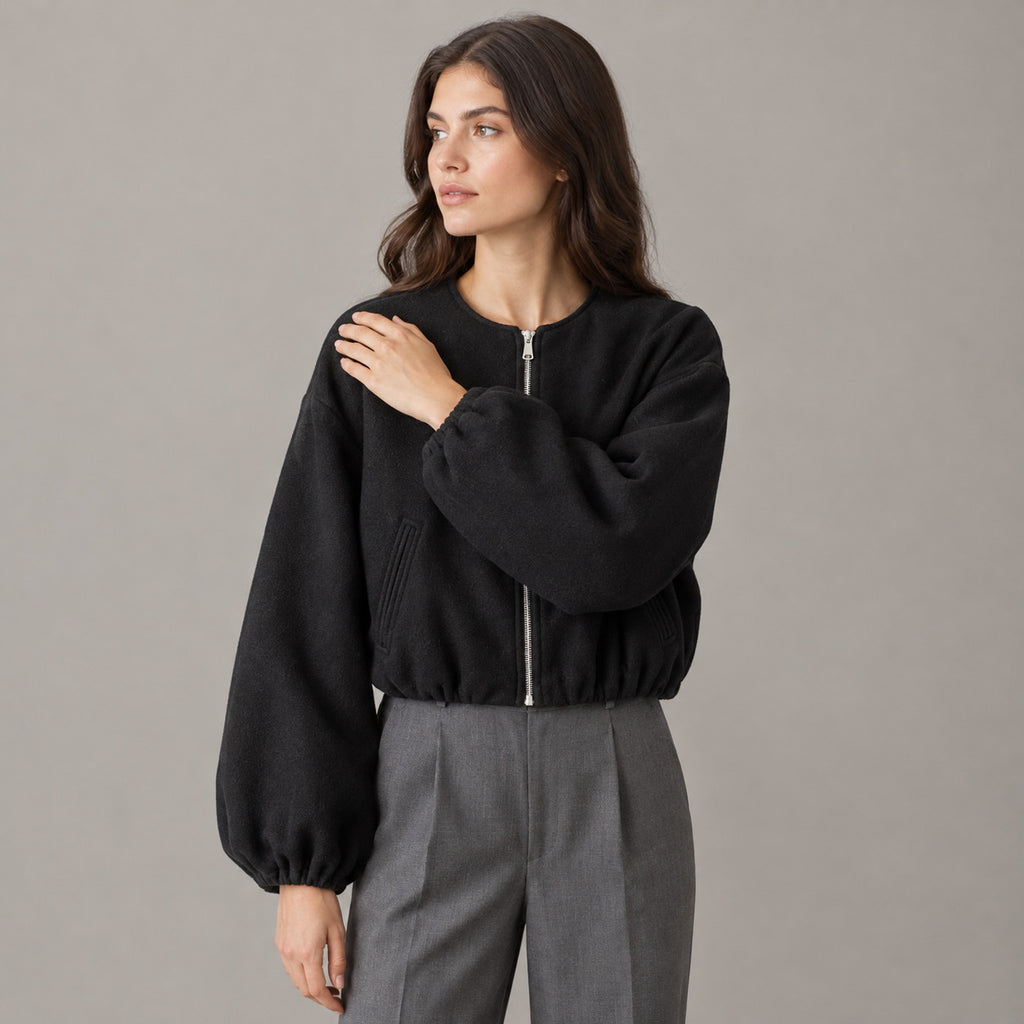 Black cropped collarless zip-up jacket worn by a model in a neutral studio.