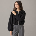 Black cropped collarless zip-up jacket worn by a model in a neutral studio.