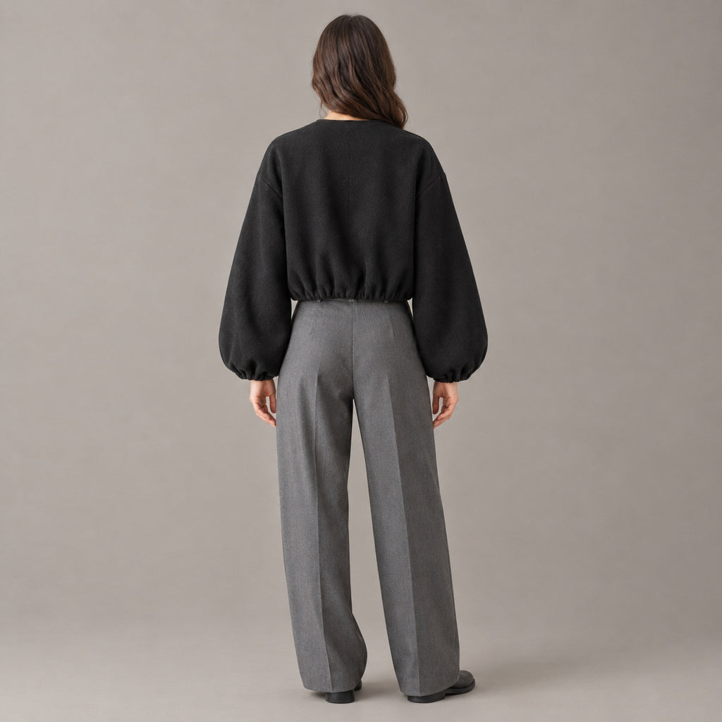 Back of the black cropped collarless zip-up jacket worn, showing the clean back and gathered hem.
