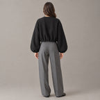 Back of the black cropped collarless zip-up jacket worn, showing the clean back and gathered hem.