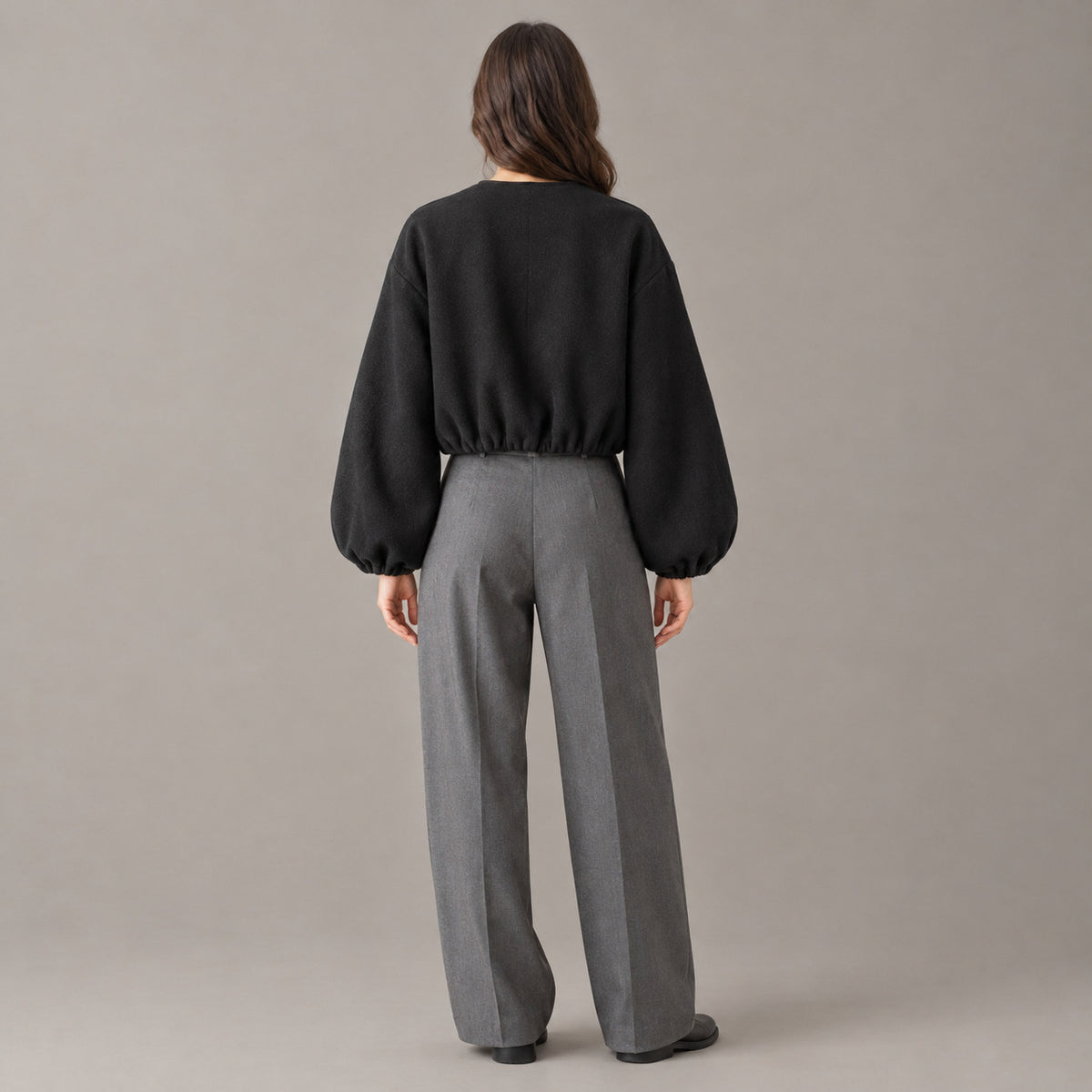 Back of the black cropped collarless zip-up jacket worn, showing the clean back and gathered hem.